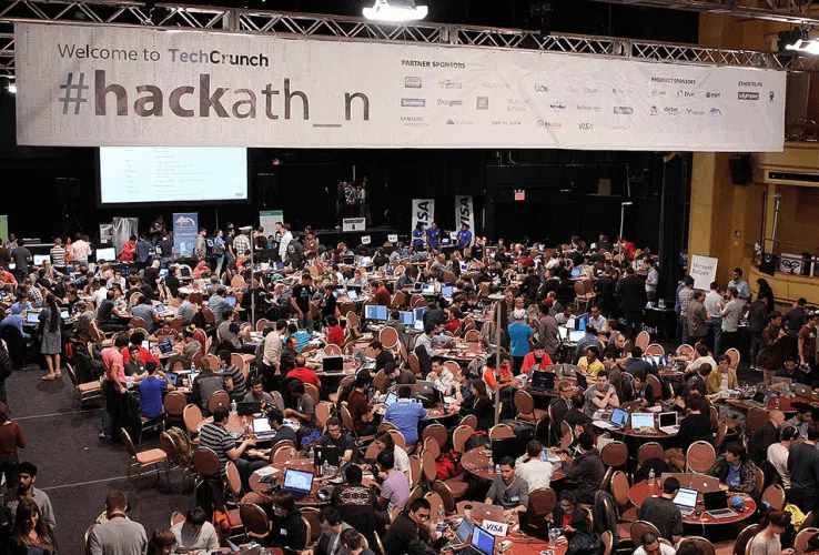 Crowded TechCrunch hackathon event with hundreds of participants working at round tables